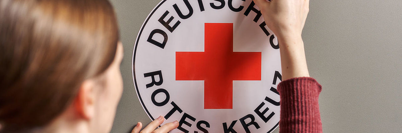Symbolfoto Frau klebt ein DRK - Rundlogo an eine Wand