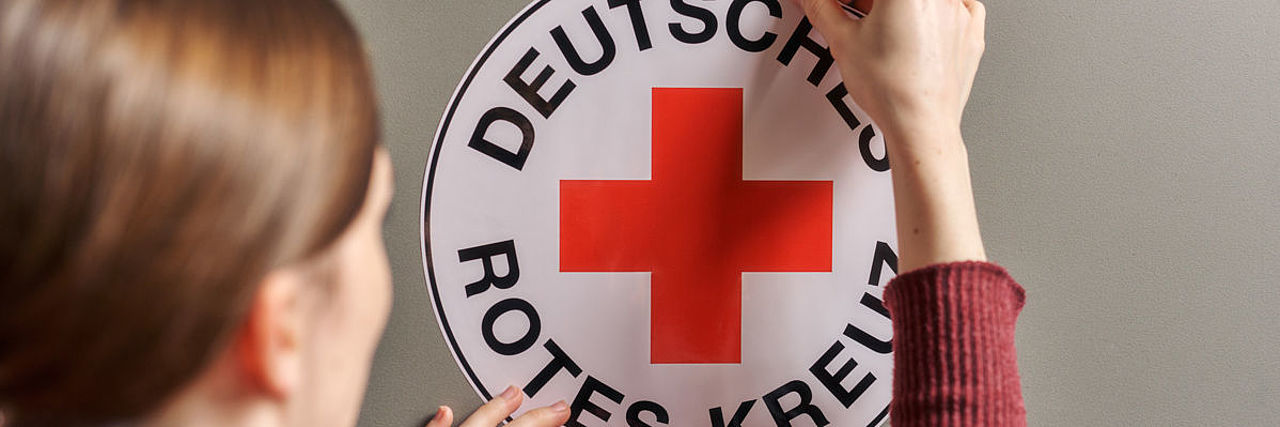 Symbolfoto Frau klebt ein DRK - Rundlogo an eine Wand