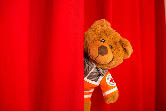 Teddybär in Einsatzbekleidung schaut aus rotem Vorhang