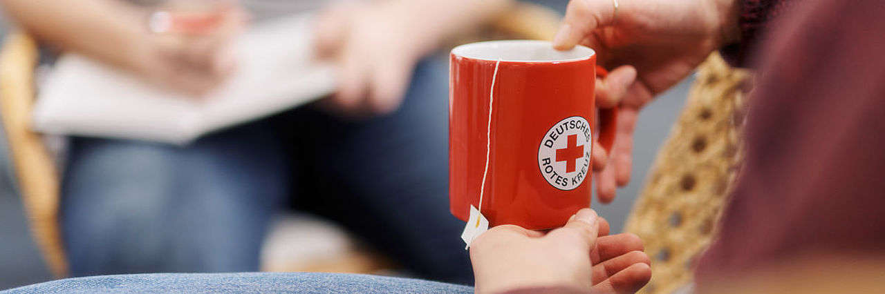 Symbolfoto Hände halten einen roten Becher mit DRK - Logo