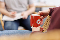Symbolfoto Hände halten einen roten Becher mit DRK - Logo