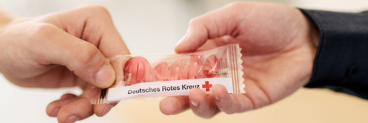 Symbolfoto, Give away des DRK, roter Weingummi in Form des Schriftzuges ‚Danke‘, in der Verpackung